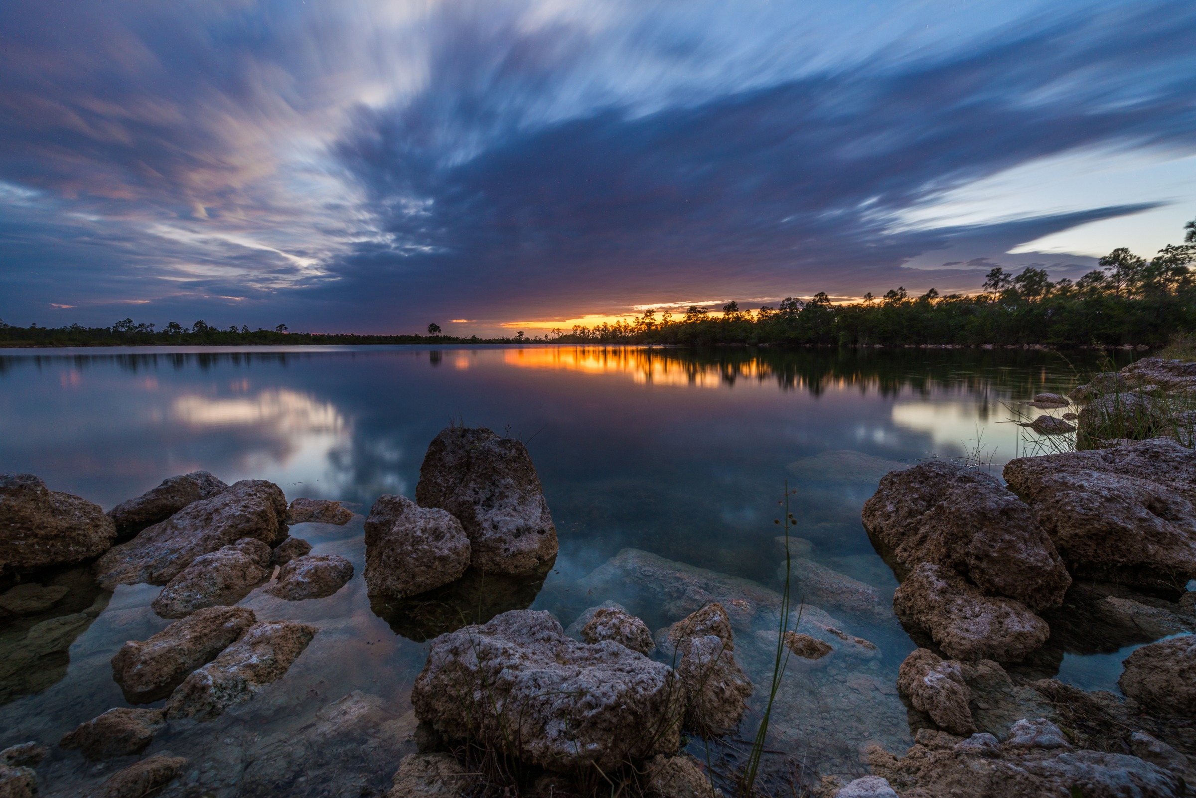 Edin Chavez Everglades collection photograph with a low bright horizon, clouds reflected in water and rocks in the foreground