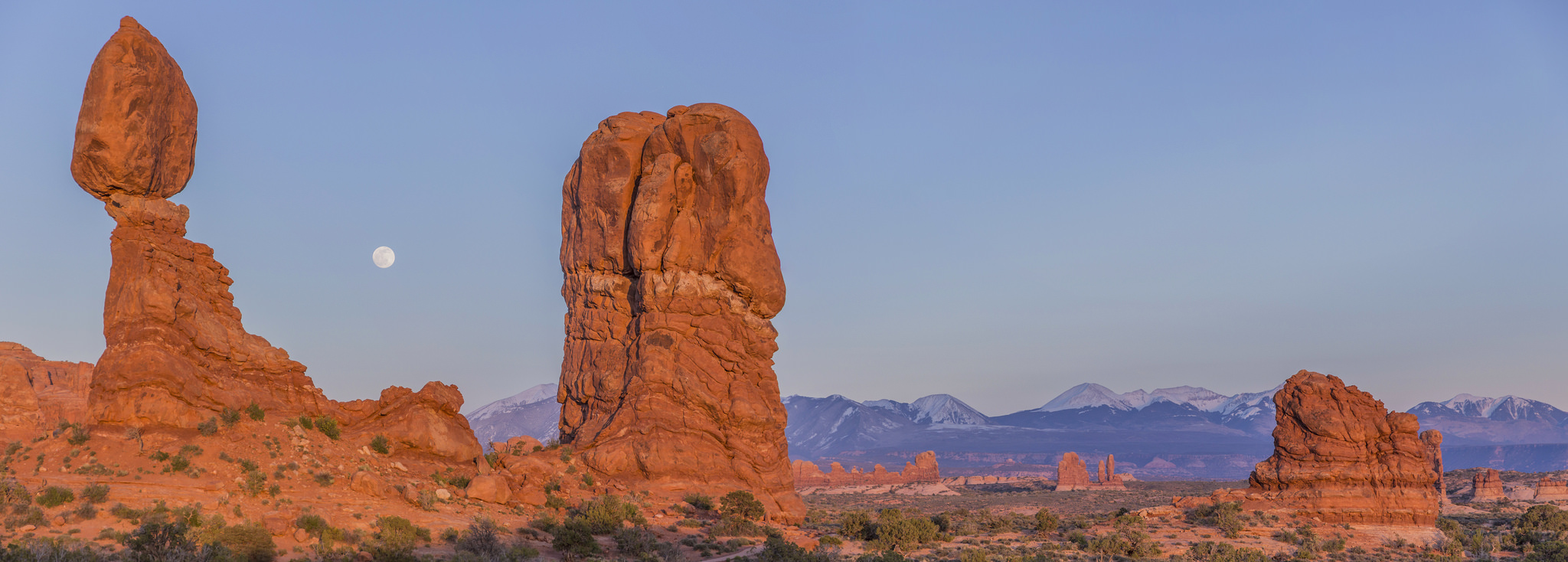 Balanced Rock with moon and distant mountains in Arches National Park