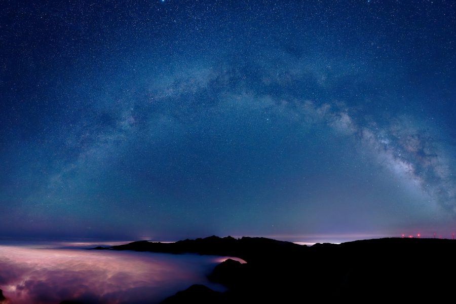 Milky Way arch and dense stars above dark mountain silhouettes and low pink clouds at night
