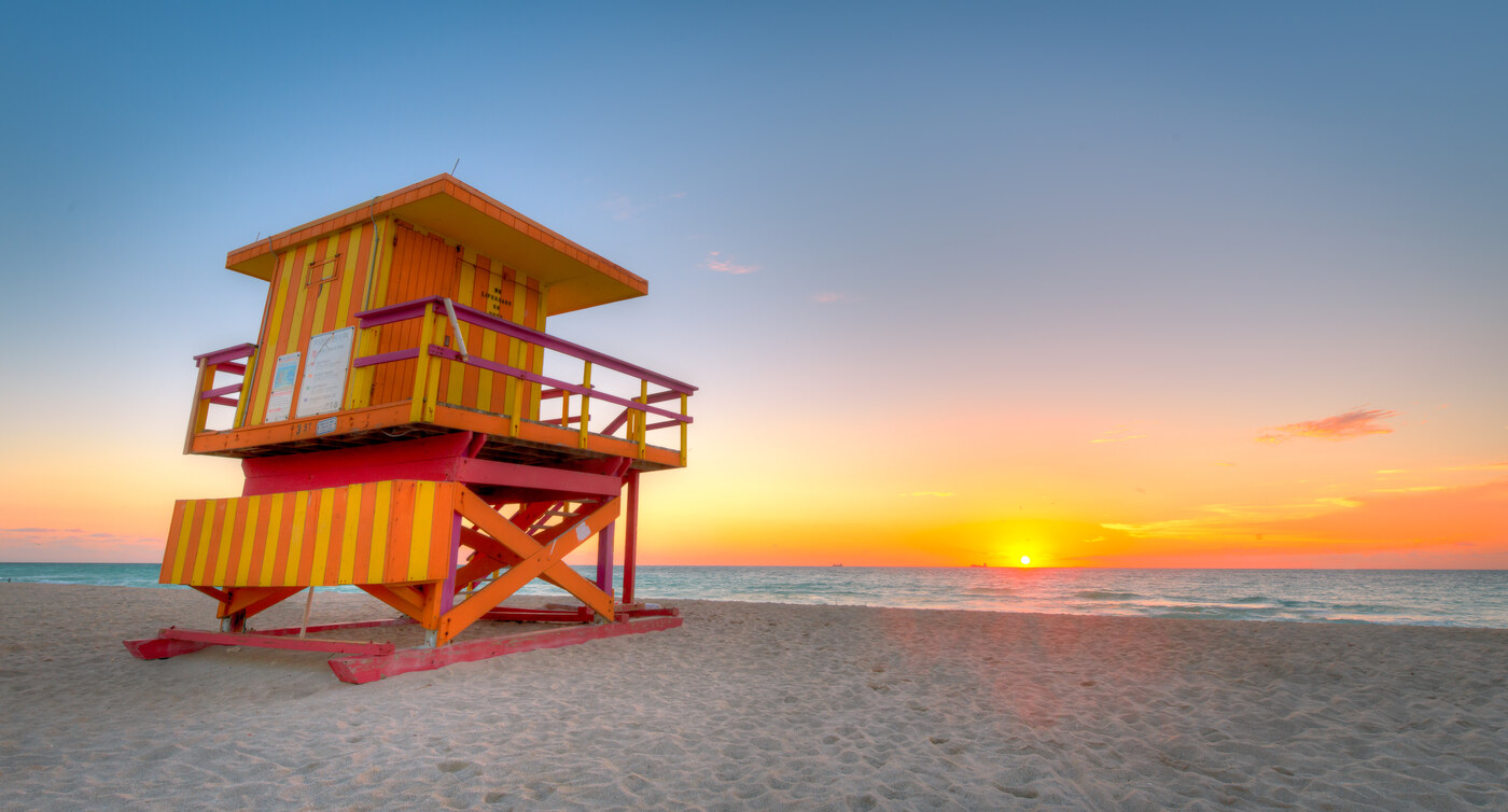 A bright orange and yellow lifeguard tower on an empty beach under a colorful sky