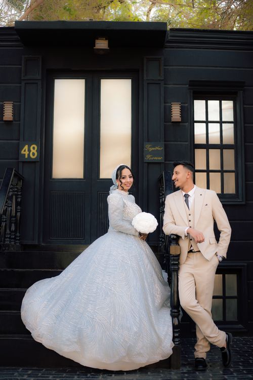 Bride and groom posing outside a dark architectural entrance with the bride's white gown spread beside them