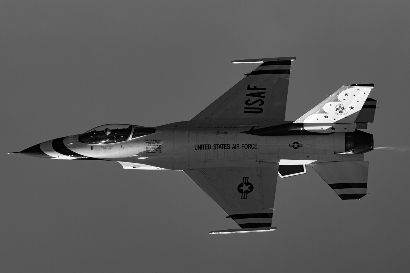 Black and white photo of a USAF Thunderbirds F-16 filling the frame from below against a clean gray sky