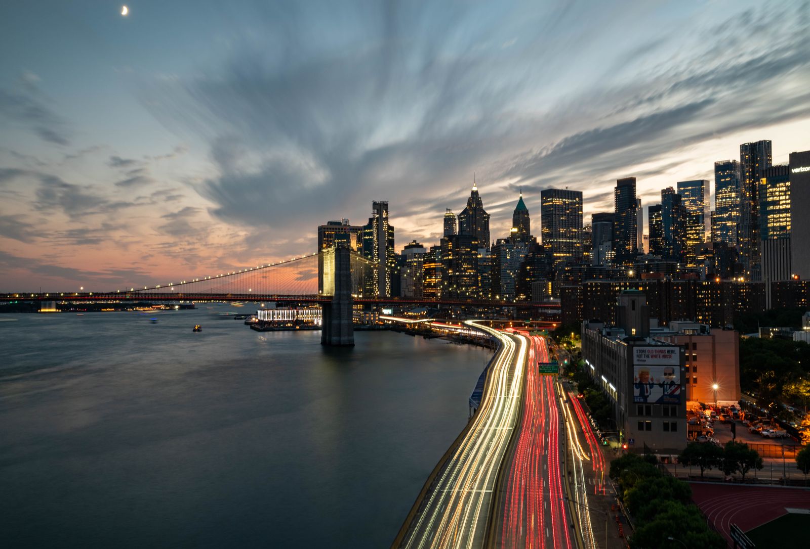 City skyline at sunset with streaky clouds and light trails from traffic beside the water