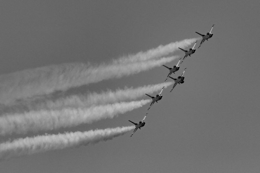 Black and white photo of USAF Thunderbirds F-16 jets in a diagonal line with long smoke trails sweeping to the left