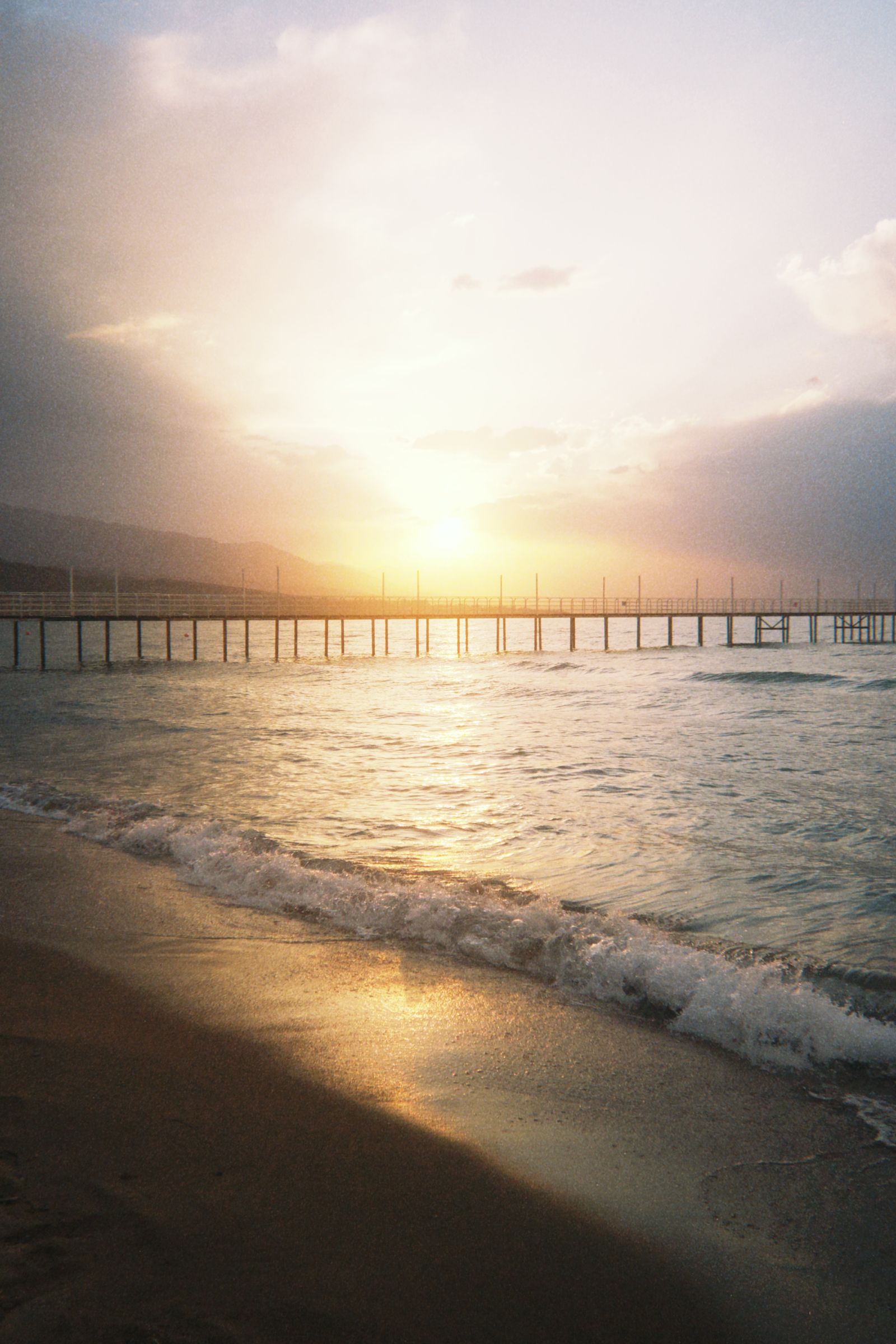 Golden sunset light over a beach with waves rolling in toward a pier