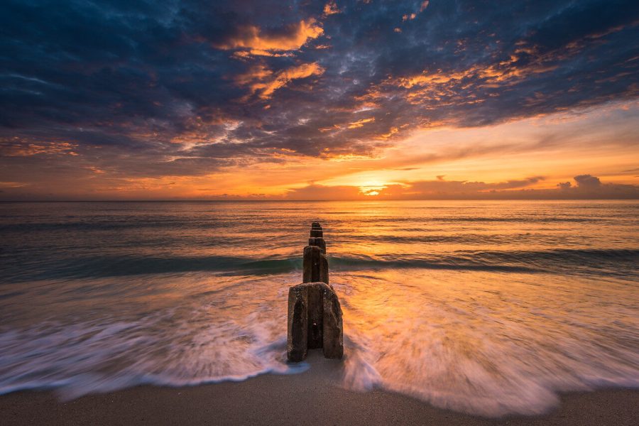 Wooden post beside breaking waves under a dramatic sunrise sky
