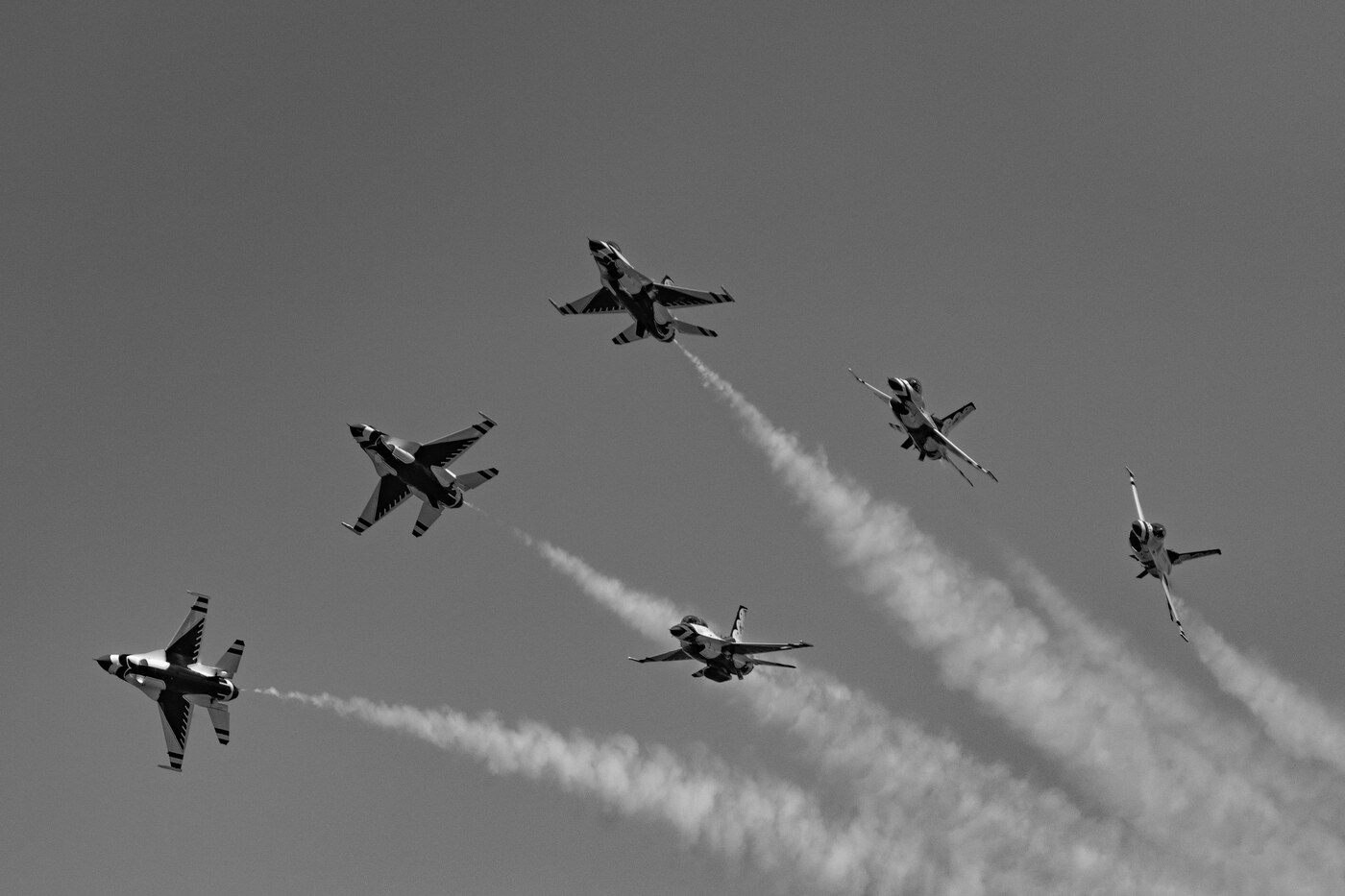 Black and white photo of six USAF Thunderbirds F-16 jets splitting apart in different directions against a gray sky with smoke trails