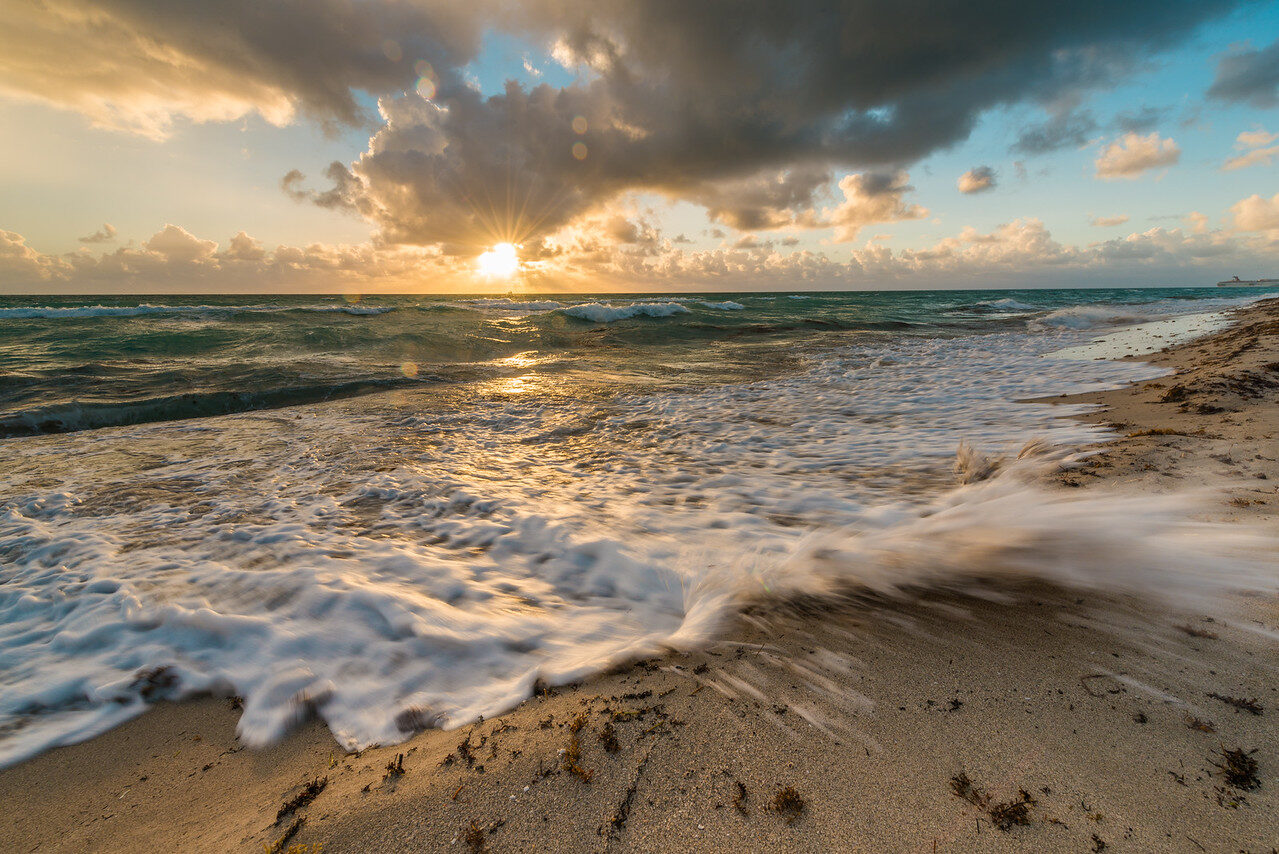 Foamy surf spreading across a sandy beach under sunrise colors