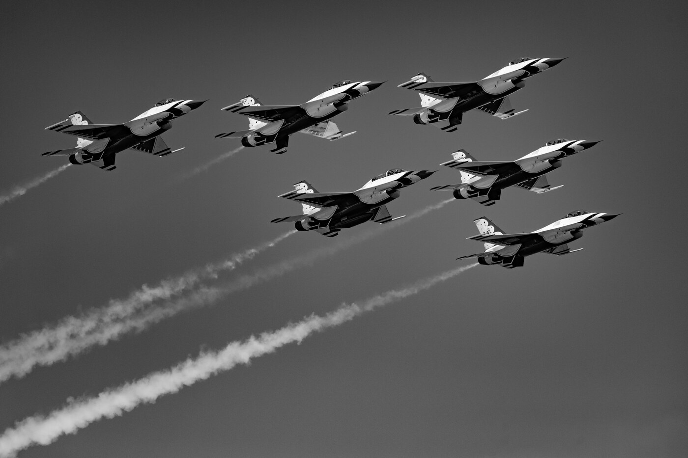 Black and white photo of six USAF Thunderbirds F-16 jets in a tight formation flying toward the upper right with smoke trails behind