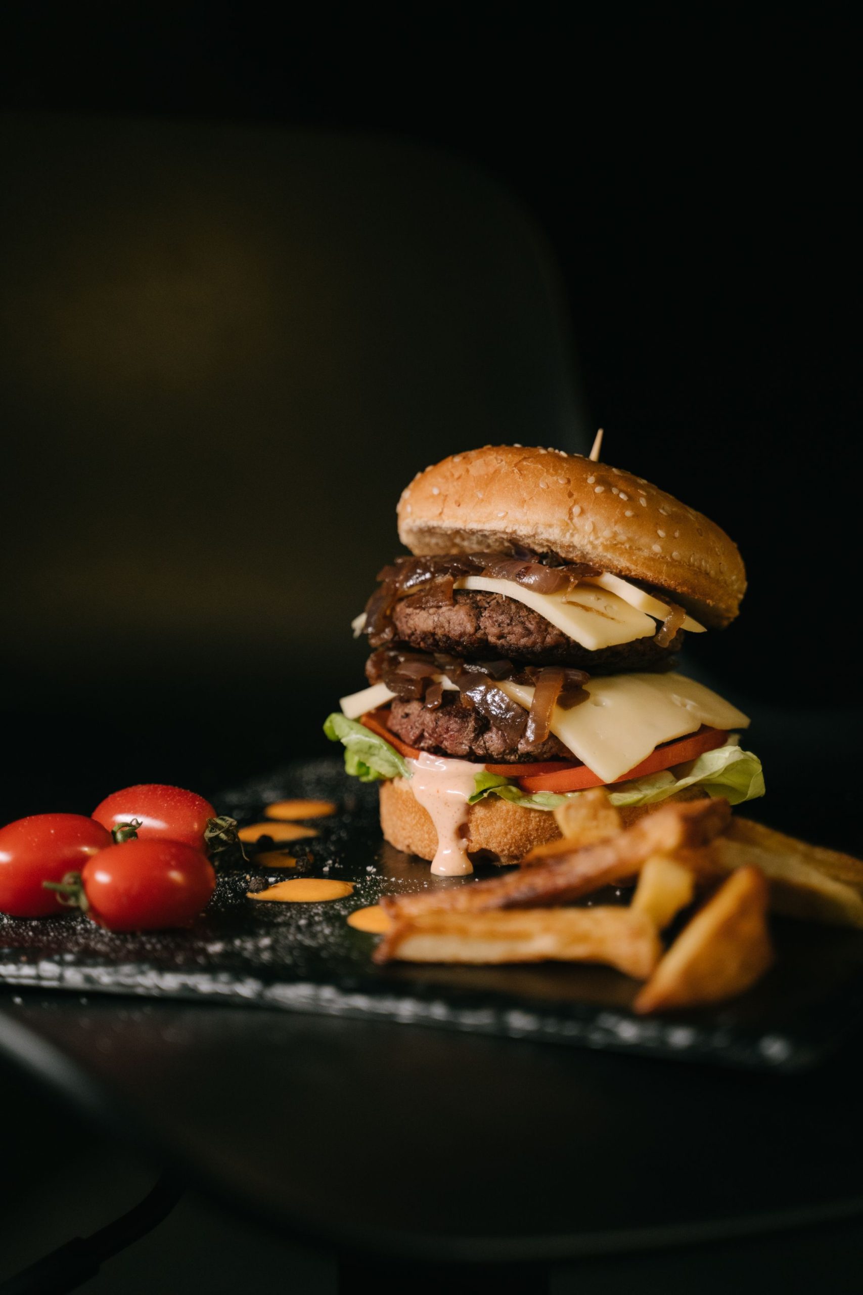 Double cheeseburger with melted cheese, onions and fries against a dark background