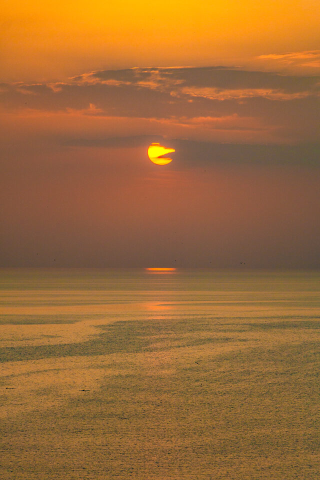 Golden sun above calm water at sunset