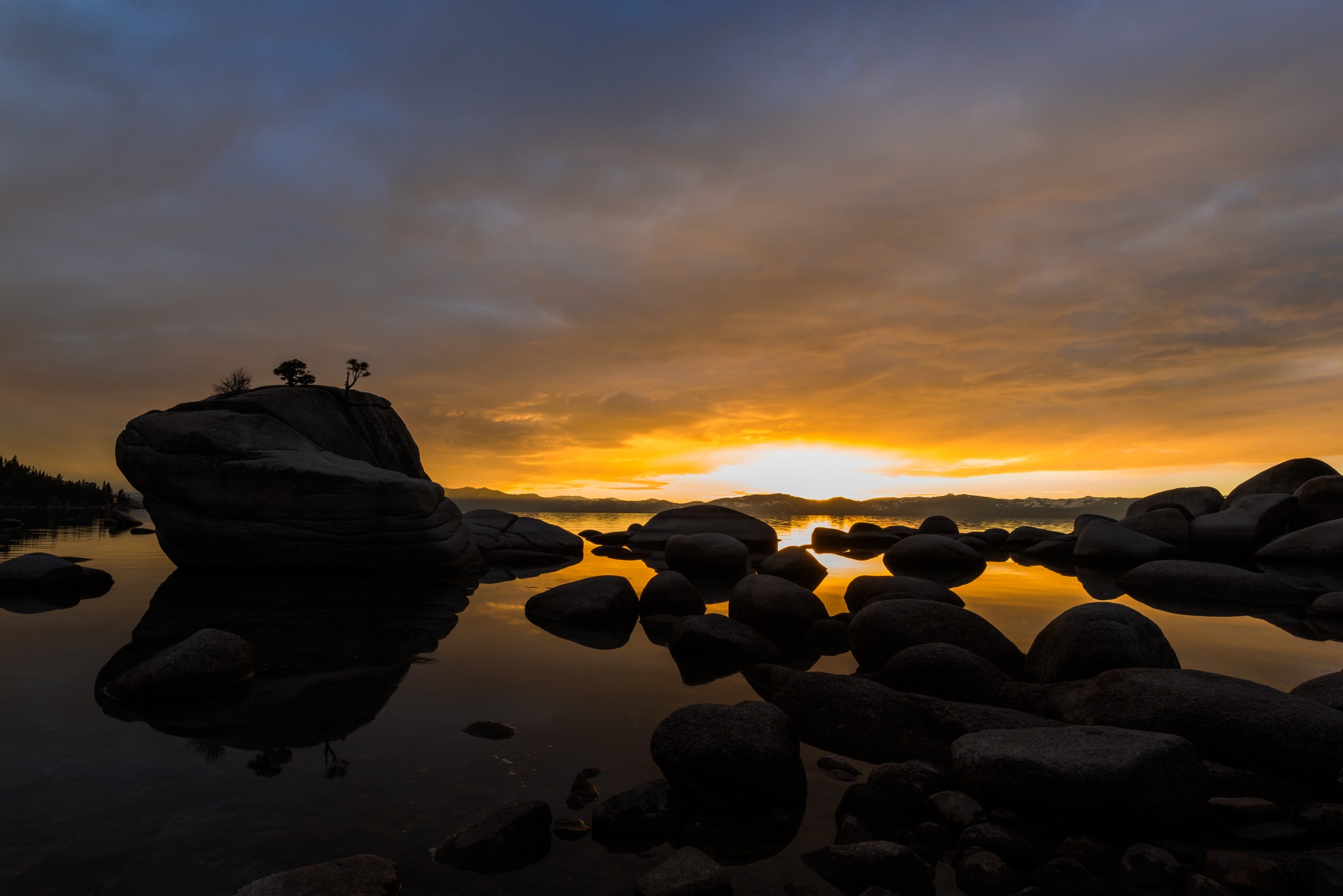 Edin Chavez Lake Tahoe Bonsai Rock photograph with silhouetted shoreline rocks and warm low light reflected in still water