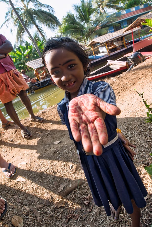 Portrait of a smiling girl in Kerala, India, holding out a hand decorated with henna, palm trees and boats behind her