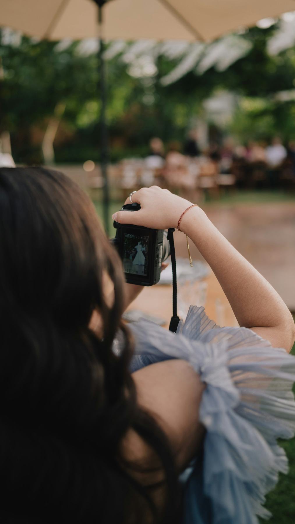 Wedding photographer holding a camera while photographing a bride at an outdoor celebration