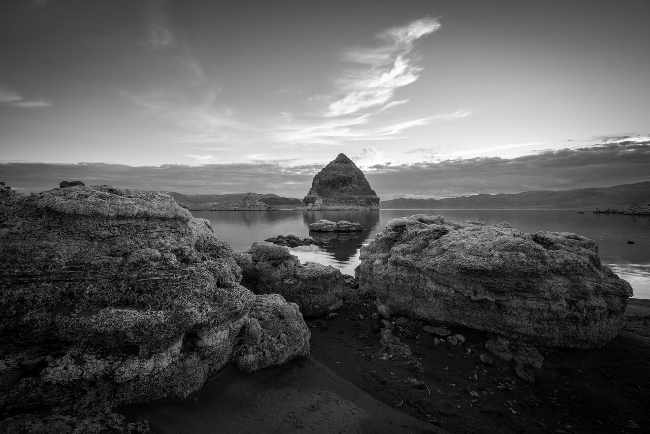 Black and white rocks beside a still lake under clouds
