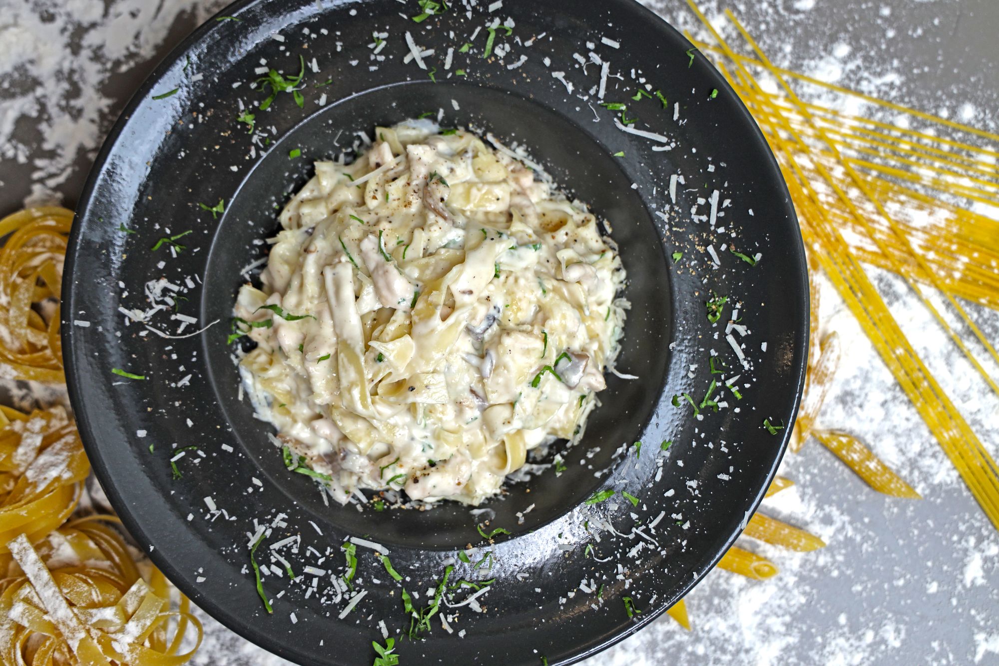 Overhead creamy mushroom pasta on a dark plate with grated cheese and herbs