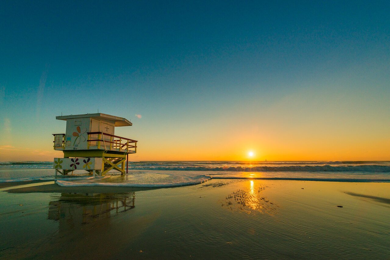 Lifeguard tower on a Miami beach with a low sun on the horizon and its reflection in wet sand