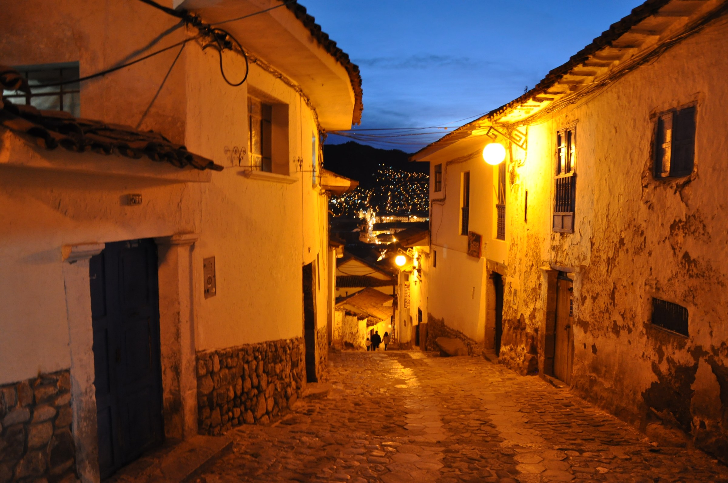 A cobbled San Blas street descending between warm-lit walls at dusk.