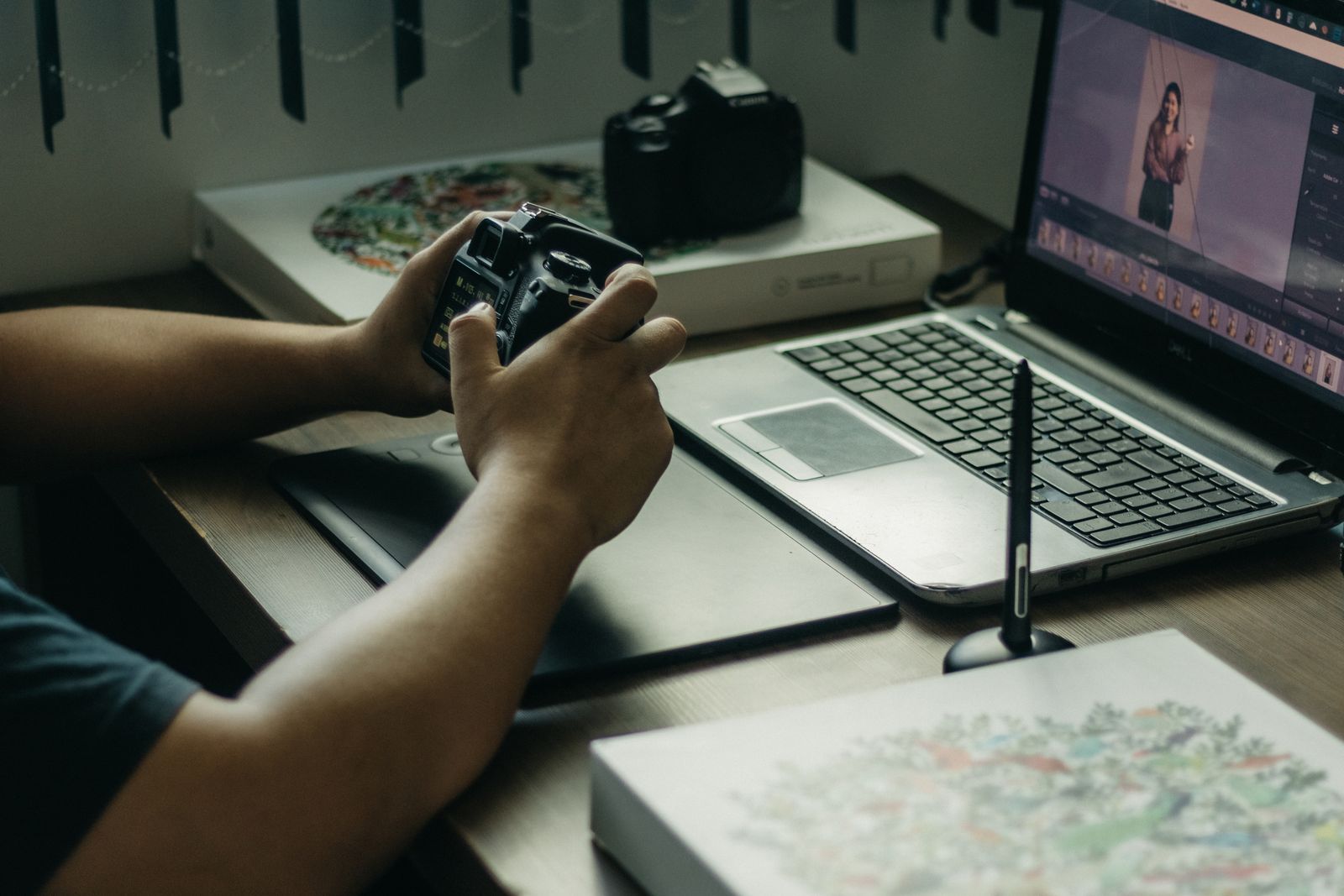 Photographer holding a camera beside a laptop and graphics tablet while editing photos in Lightroom Classic