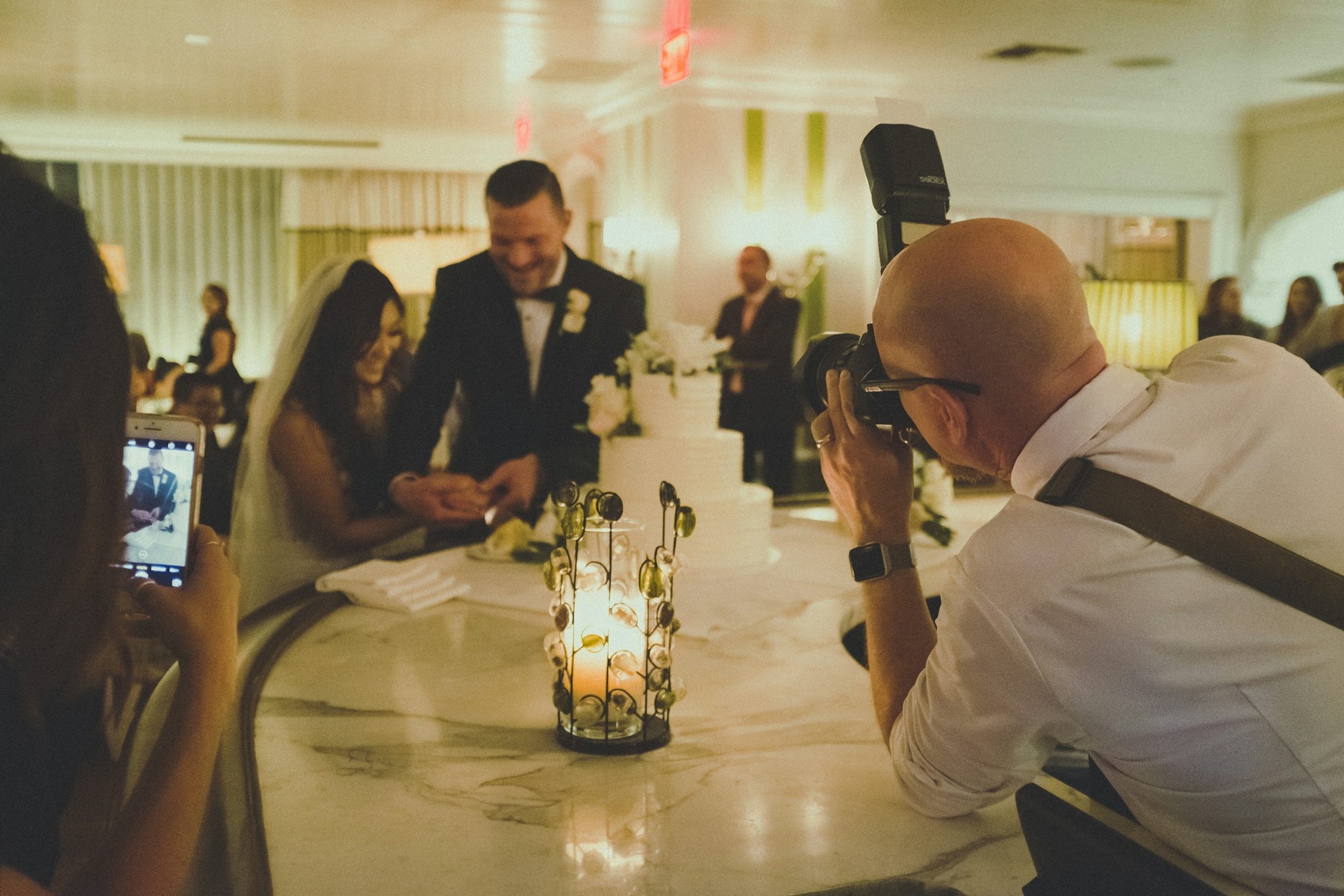 Photographer using an on-camera flash to photograph a wedding couple at an indoor reception