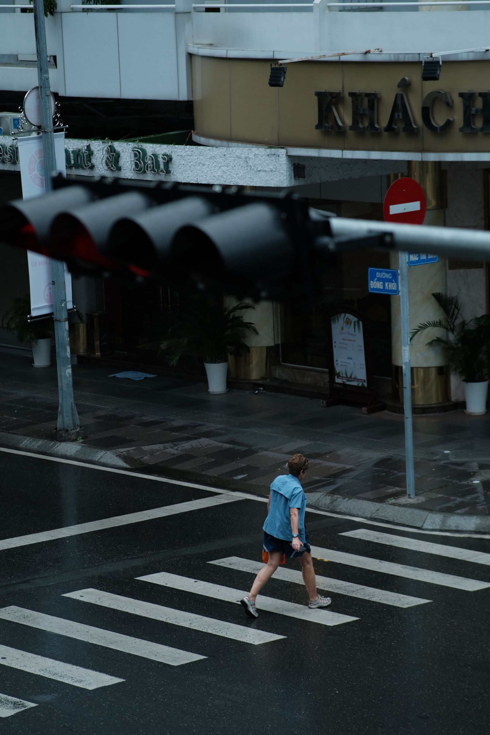 Person crossing a dark wet city street beside cafes