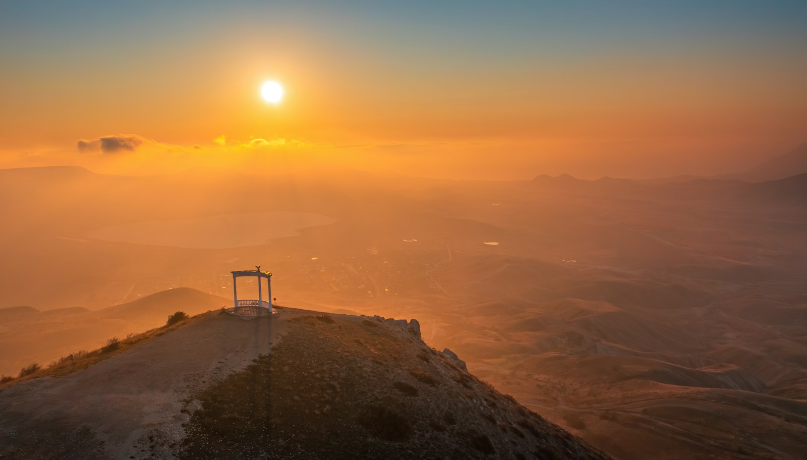 Golden sunrise over misty mountain ridges with a small viewing pavilion on a hilltop