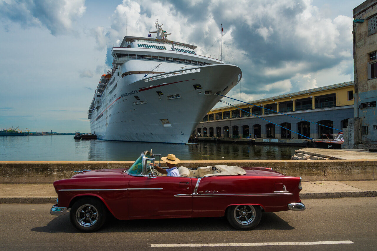 Cruise ship docked beyond a red vintage convertible in Havana, Cuba, photographed by Edin Chavez