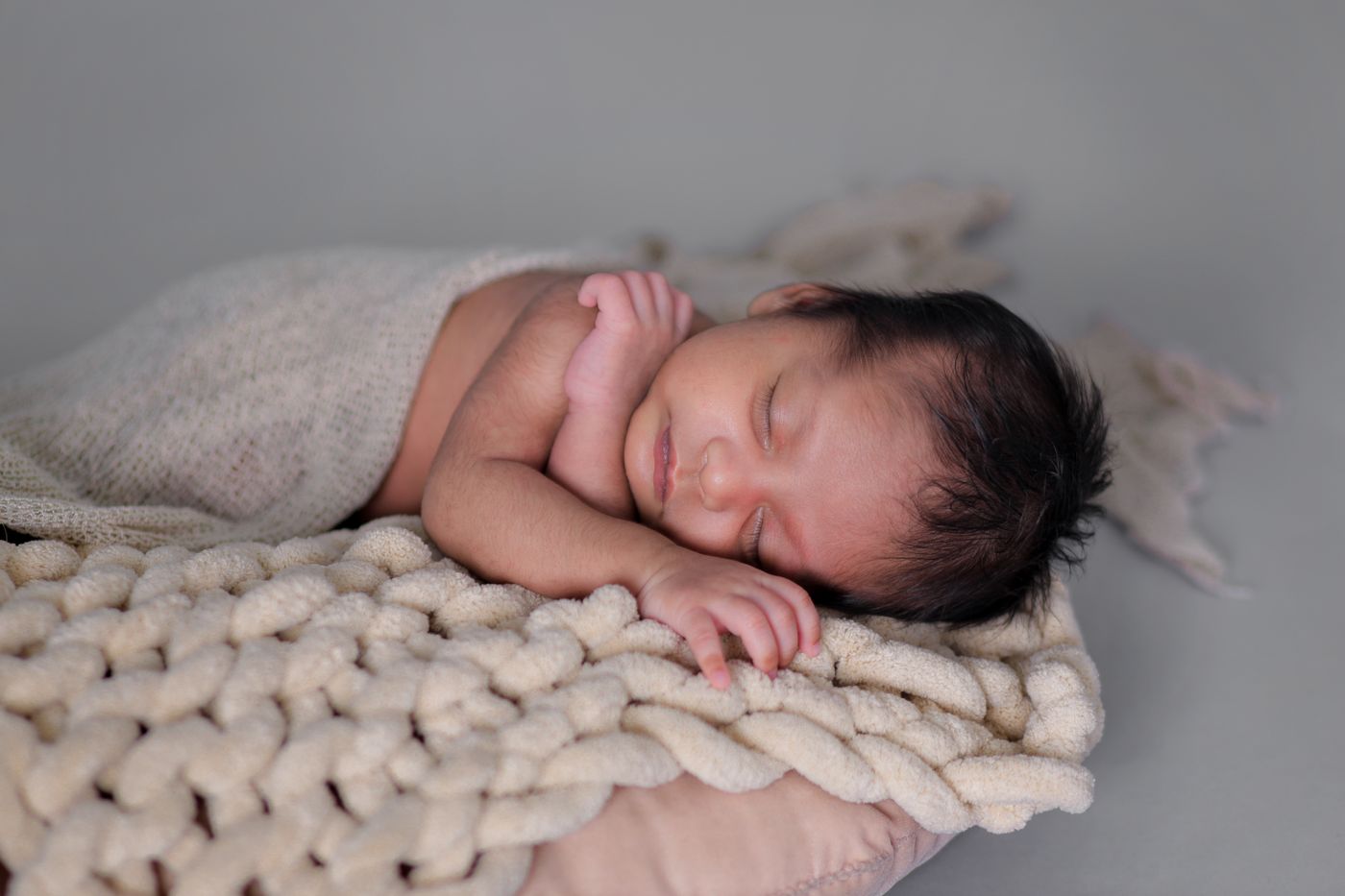 Newborn baby sleeping on a chunky knit blanket in soft studio light