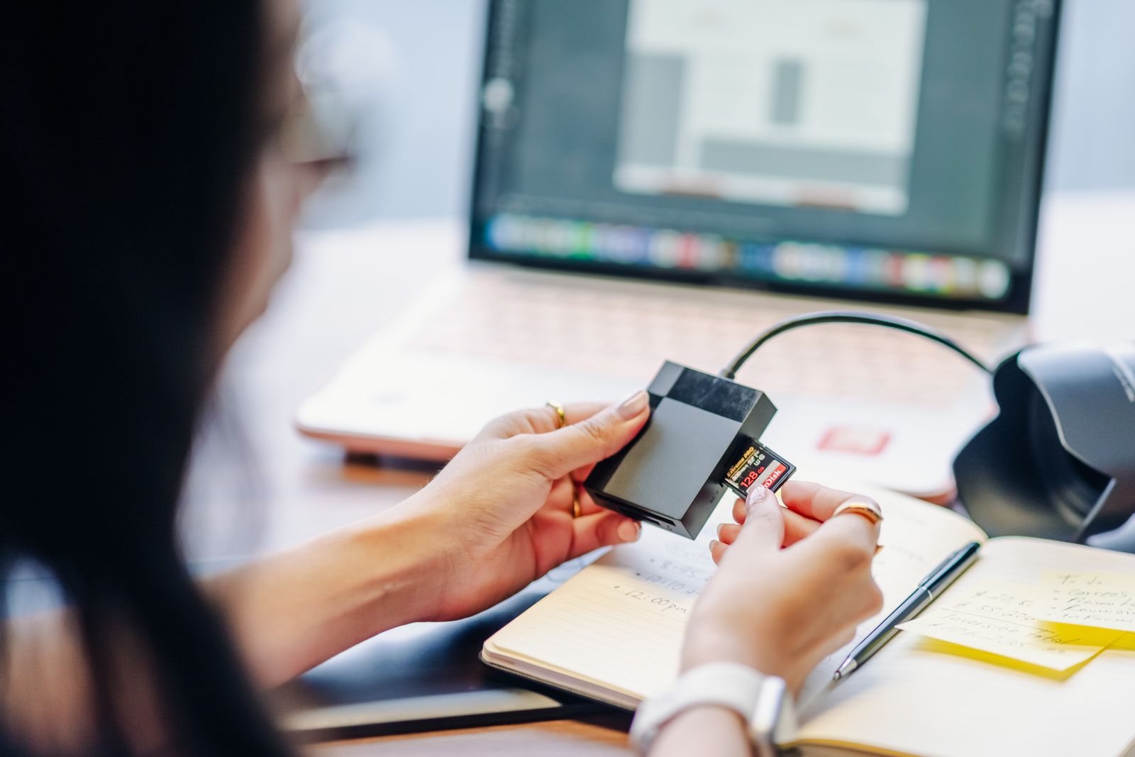 Person inserting an SD card into a card reader next to a laptop to import photos