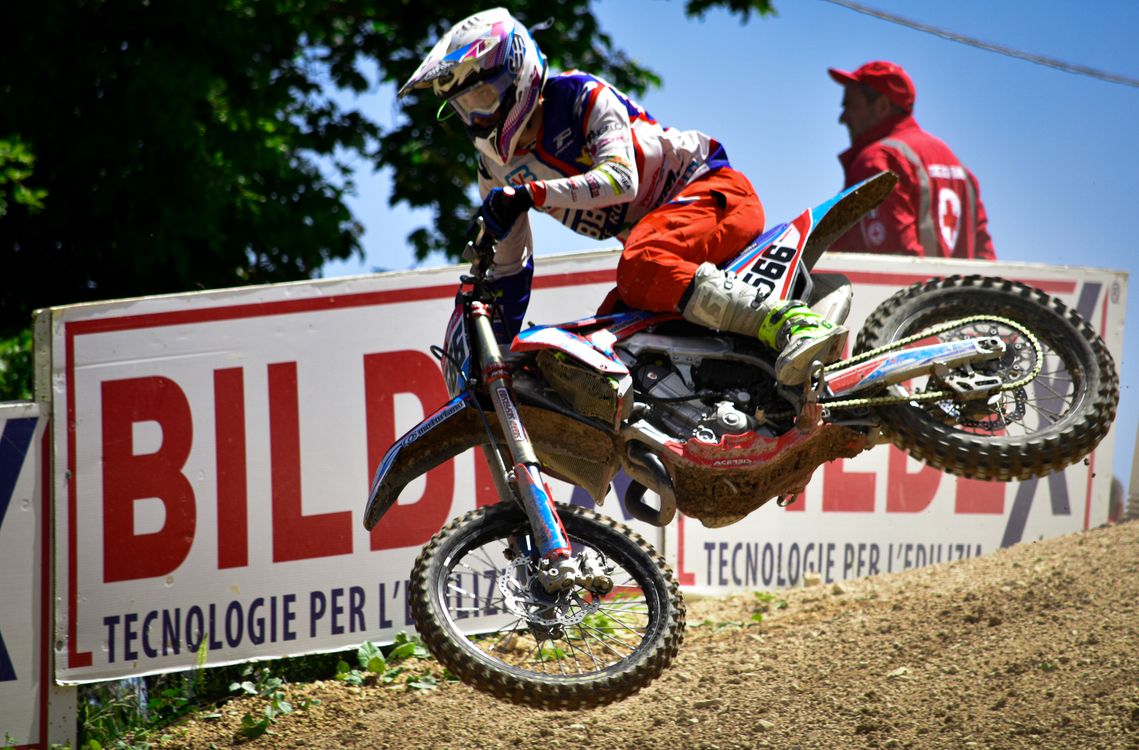 Helmeted motocross rider and dirt bike airborne above a dirt track.