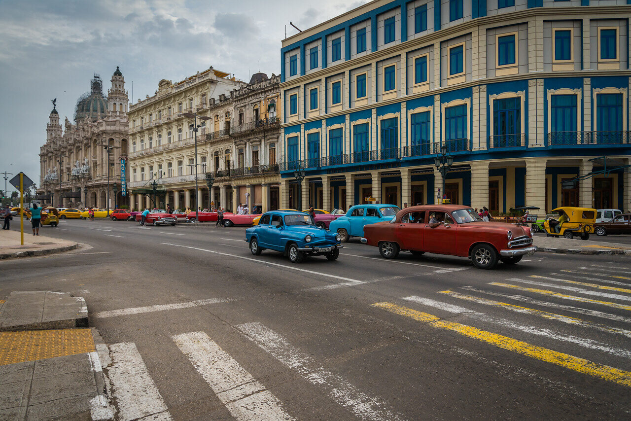 Vintage cars driving down a Havana street lined with colonial buildings, Cuba, photographed by Edin Chavez