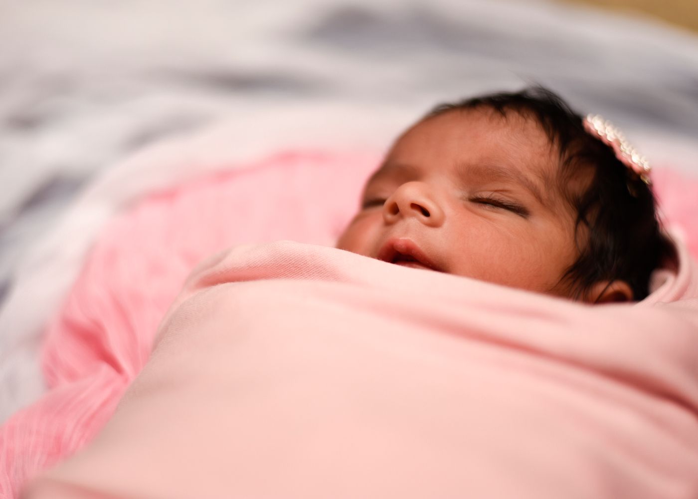 Newborn asleep in a pink swaddle, close-up