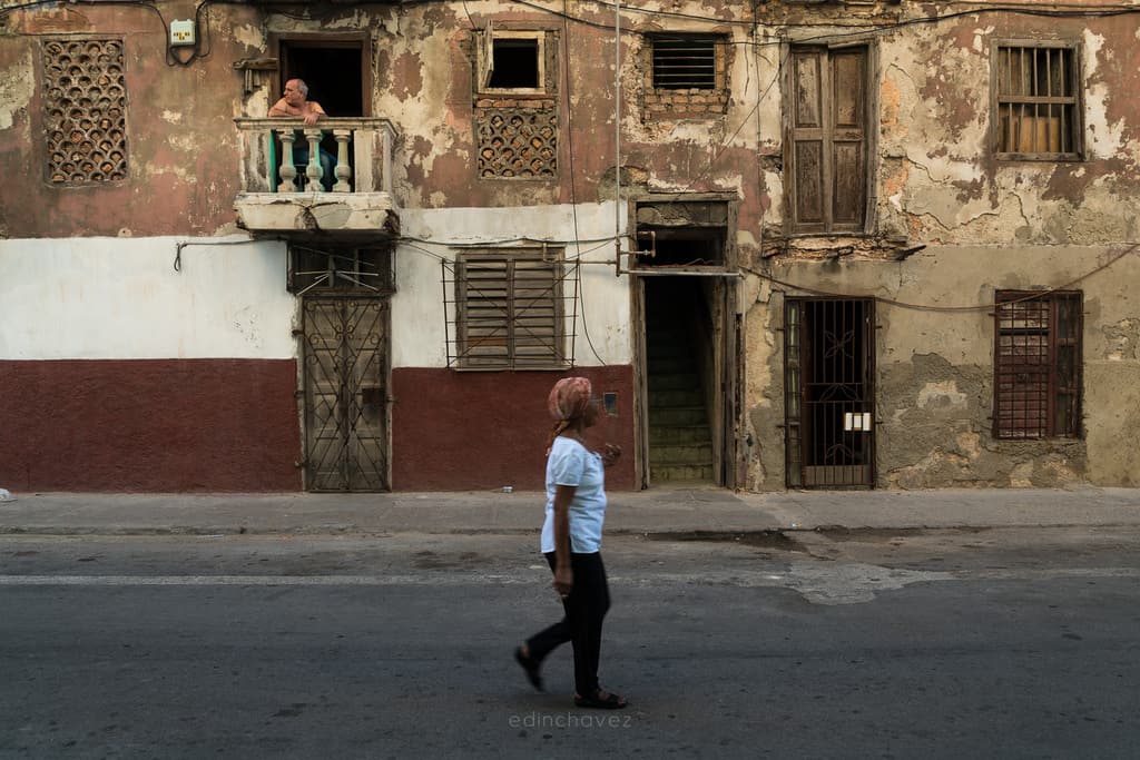 Pedestrian crossing in front of a weathered Havana building with someone on a balcony