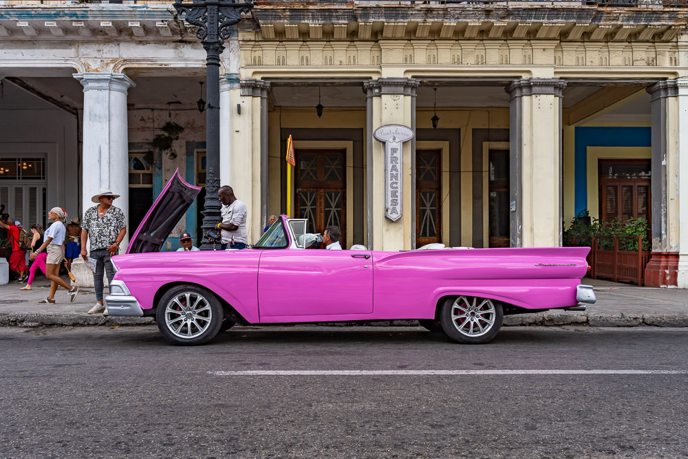 Pink vintage convertible beside pedestrians and a columned Havana building