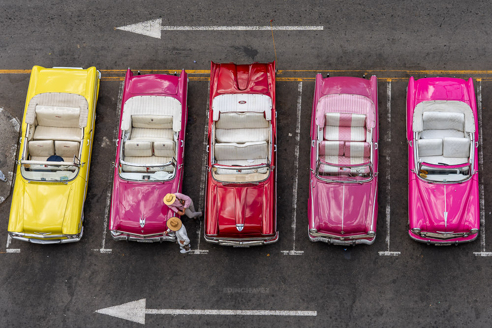 Overhead view of five colorful parked convertibles, two pedestrians and road arrows