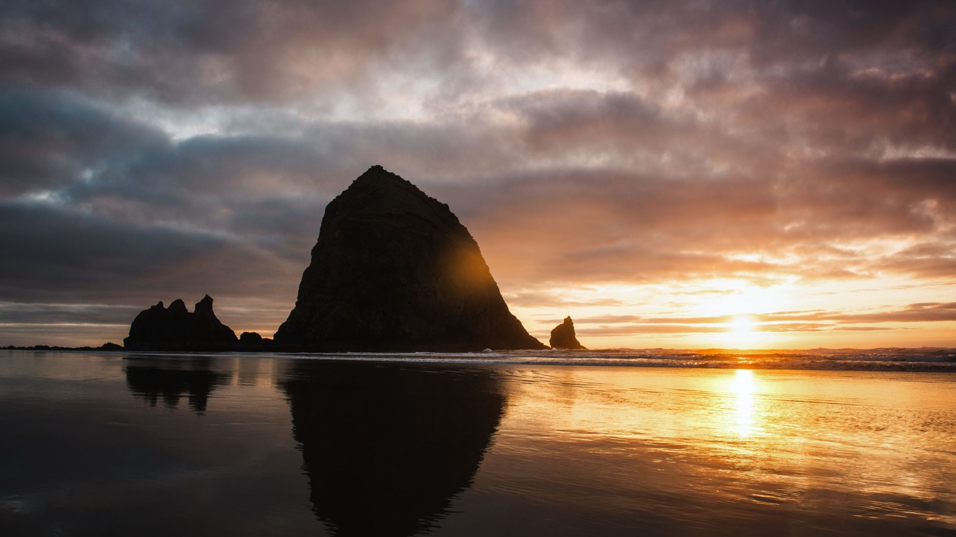 Haystack Rock silhouette and reflection under a sunset sky