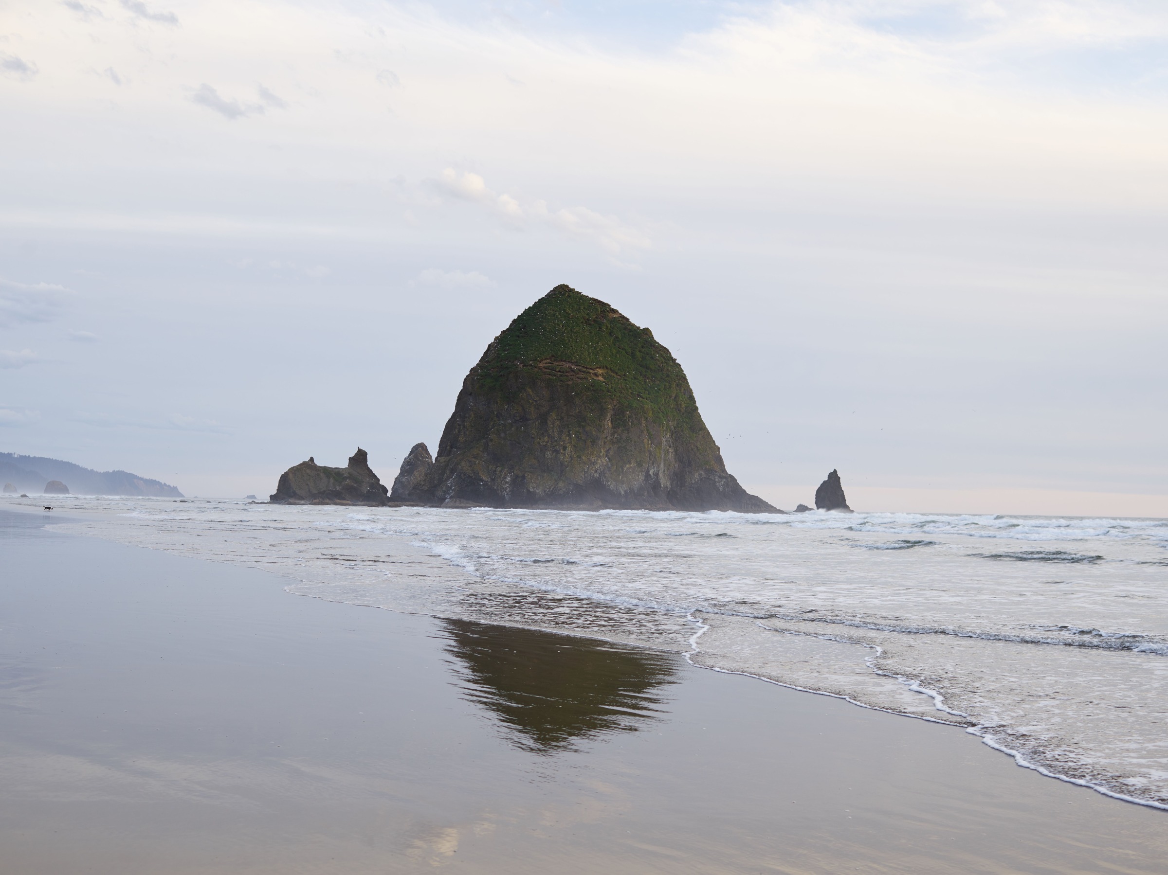 Haystack Rock with breaking surf and a partial wet-sand reflection