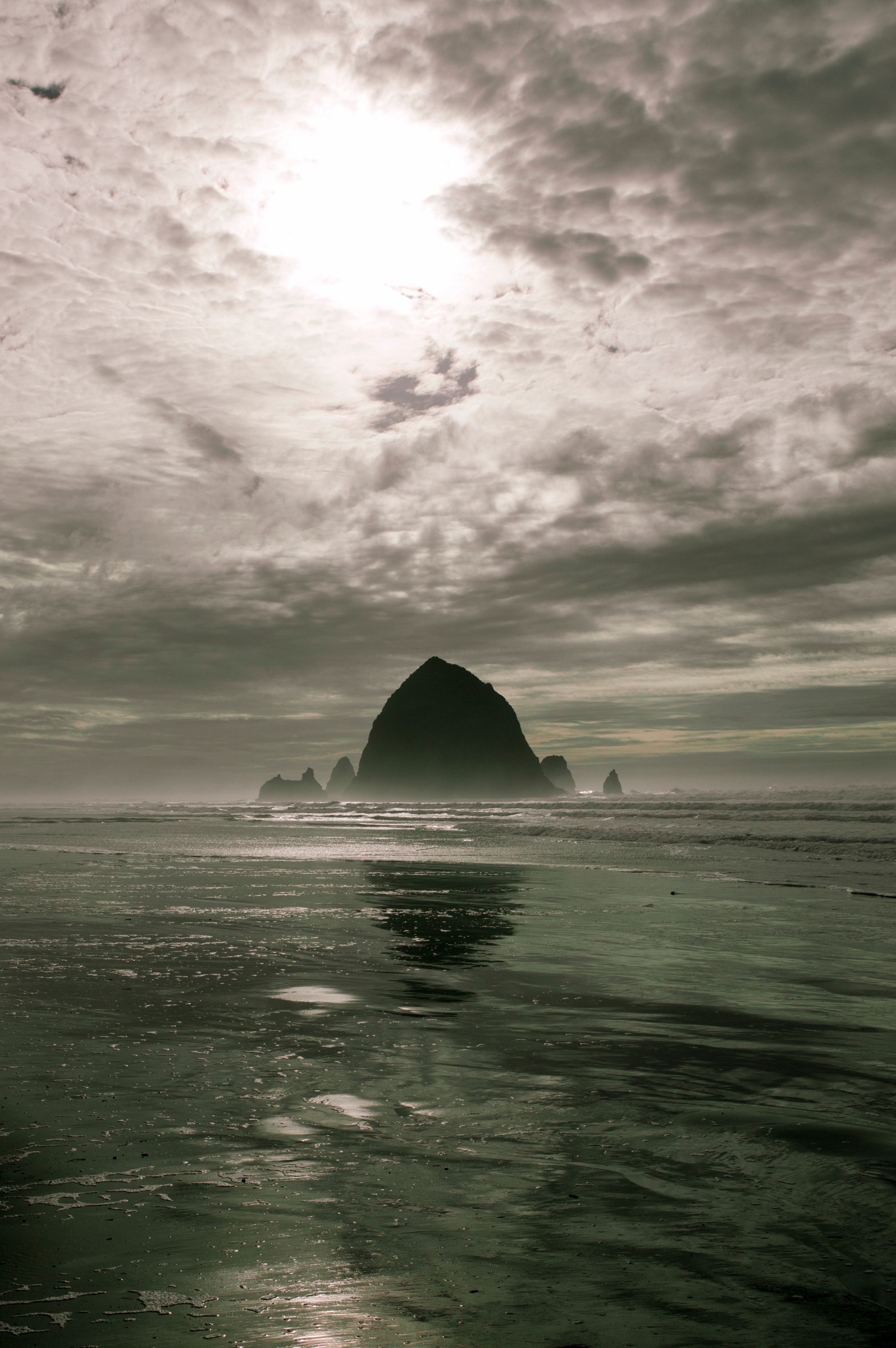 Haystack Rock silhouette beneath textured clouds in a vertical frame