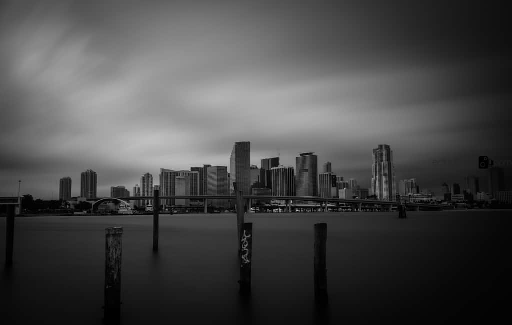 Monochrome Miami skyline across smooth water beneath clouds