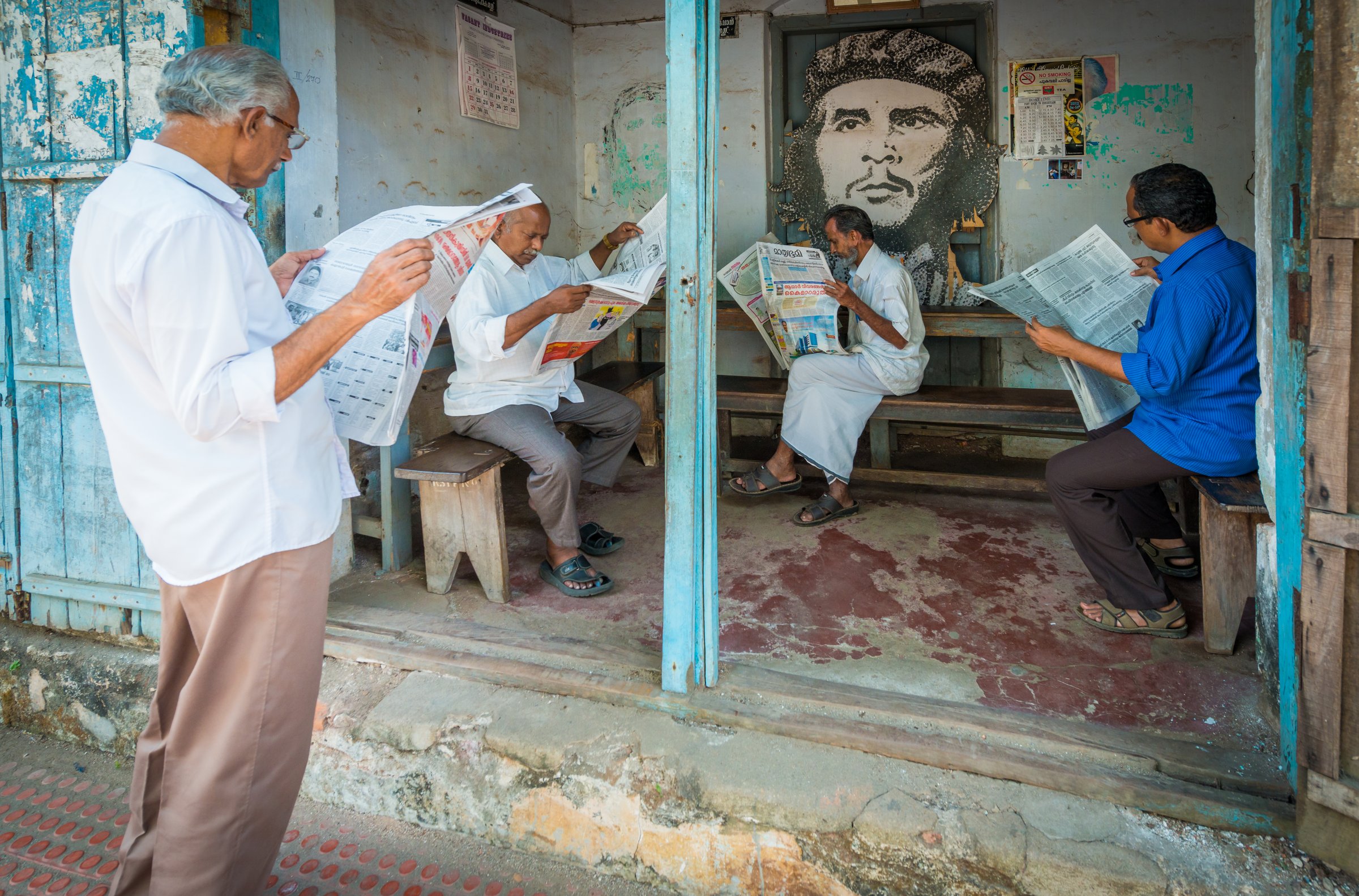Men reading newspapers by a window in India, subjects directed into the available light