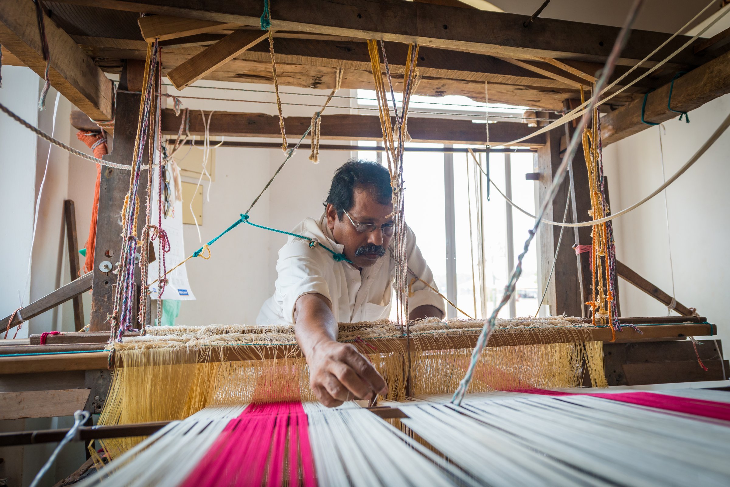 A weaver working at a window in India, soft directional light falling across the loom