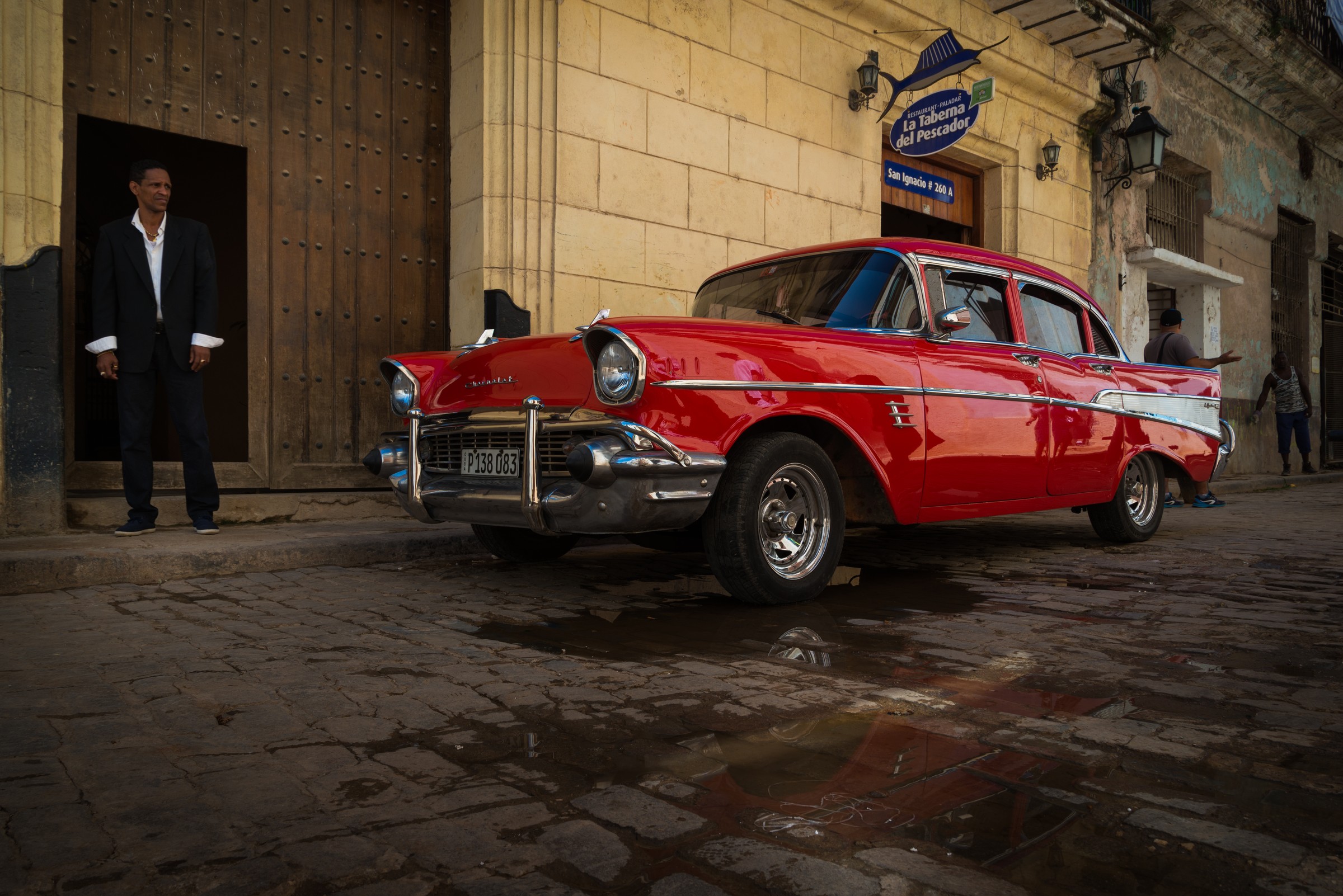 A classic red Chevrolet parked outside a Havana bar at dusk, its chrome bumper the kind of sharp edge to check at 100 percent zoom when judging noise reduction