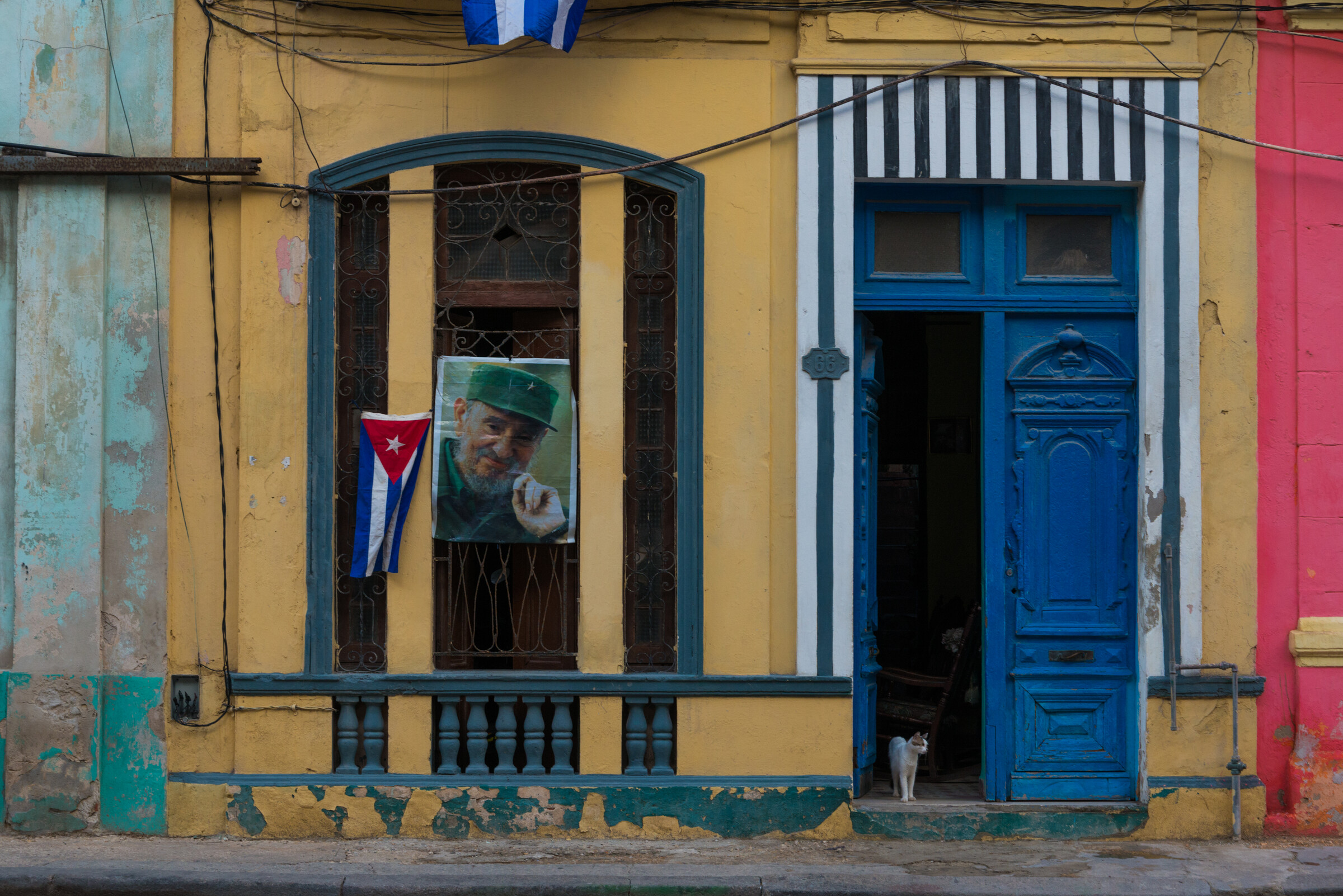 A weathered Havana doorway in yellow, blue and pink with a Cuban flag