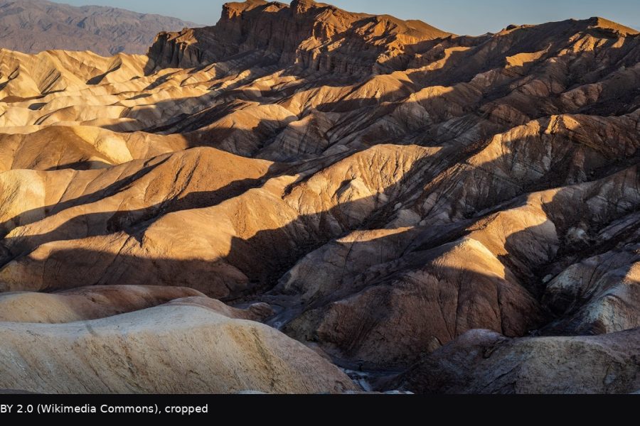 Golden sunrise raking the badlands with Manly Beacon lit, per the Commons title.