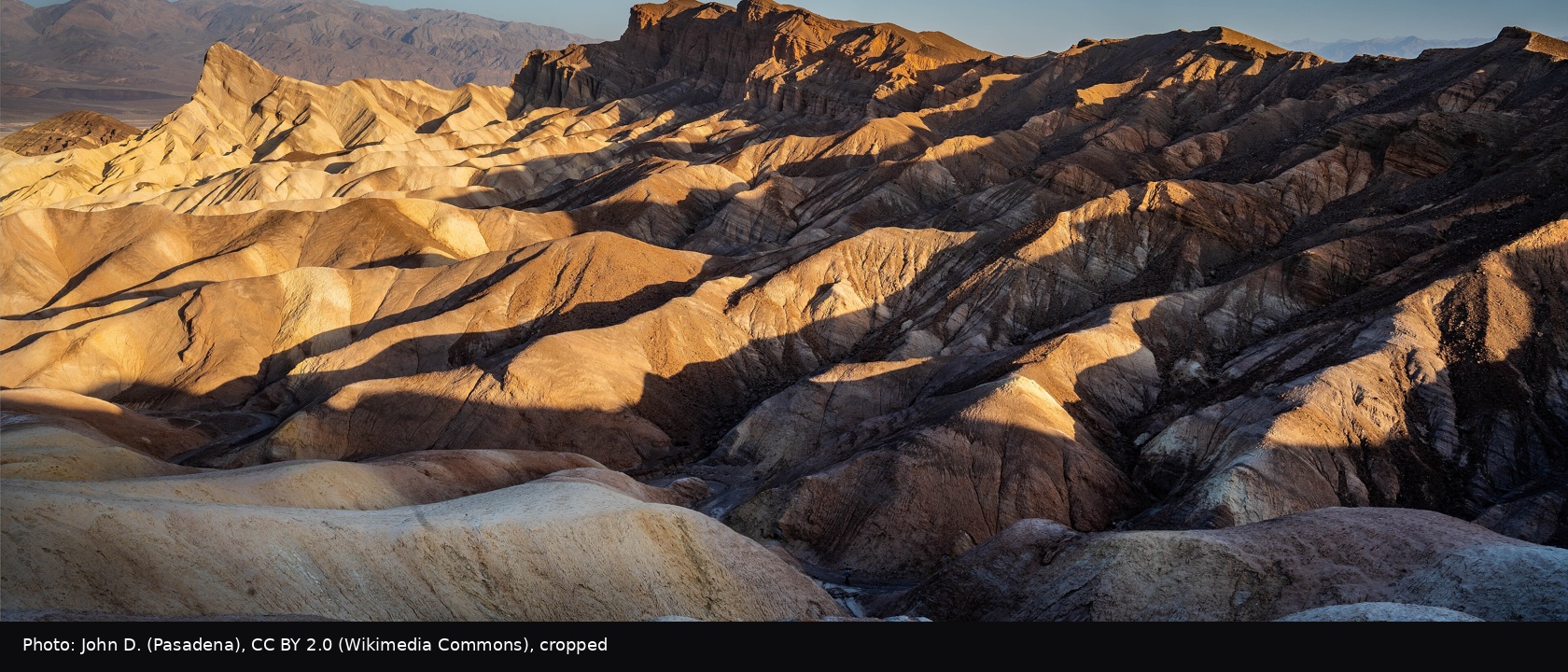Golden sunrise raking the badlands with Manly Beacon lit, per the Commons title.