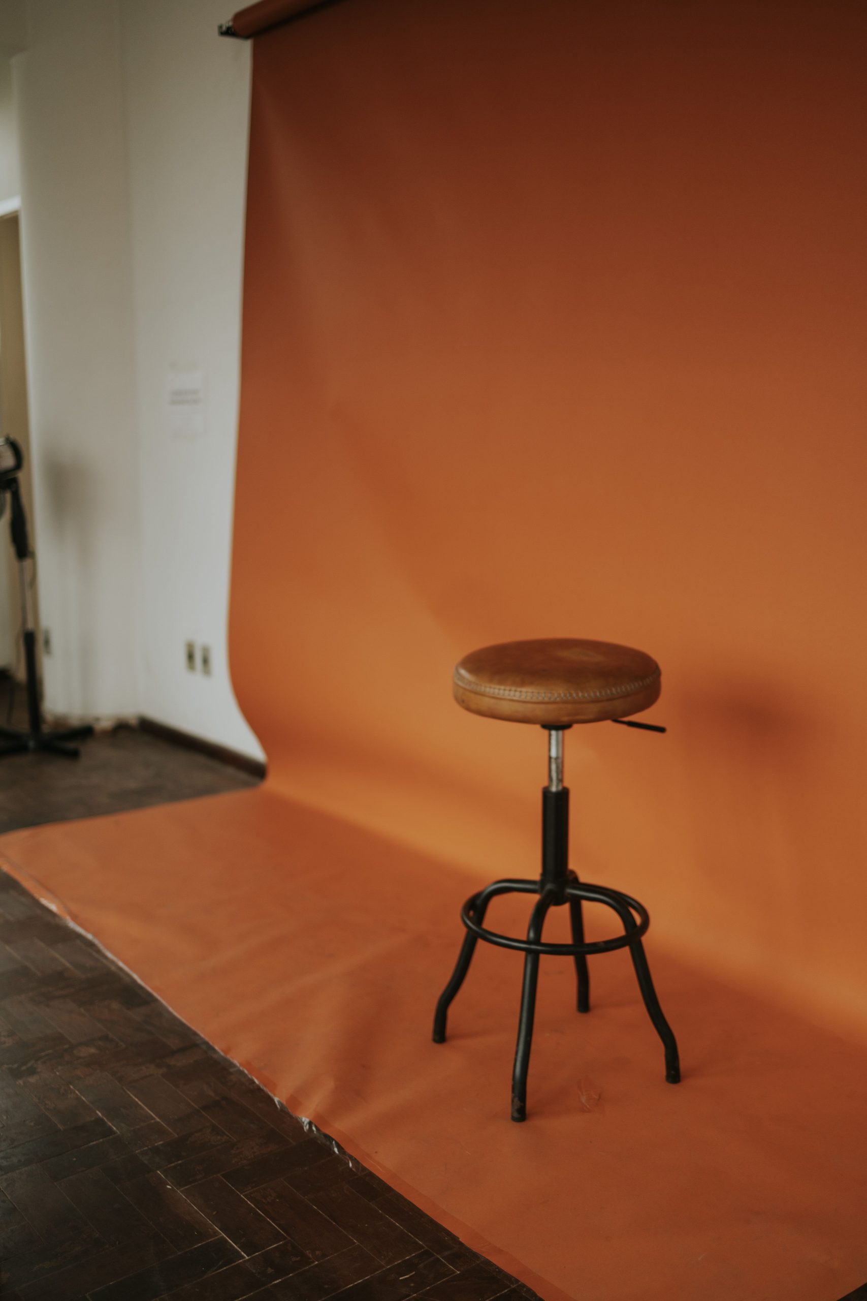 An orange backdrop with a wooden stool arranged for a minimalist portrait setup