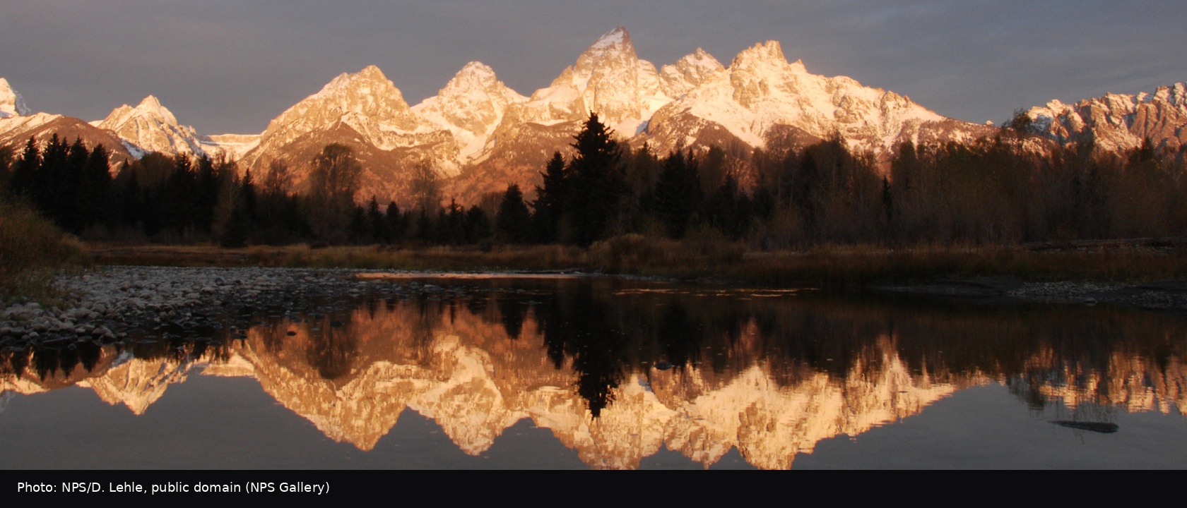 The Teton range mirrored in a still slough below the peaks, per the NPS title.
