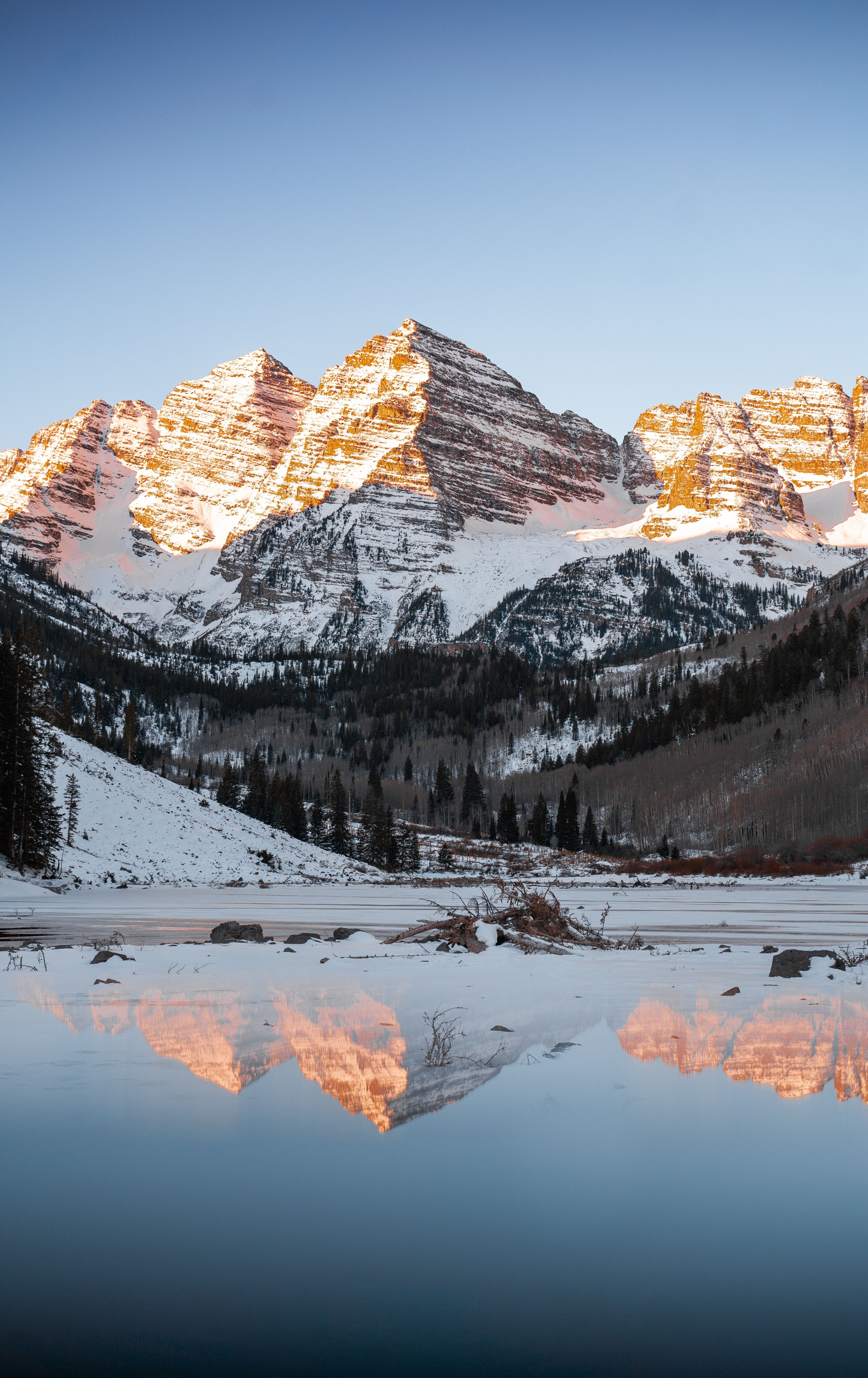 Snow-covered Maroon Bells in warm light above a partly frozen lake