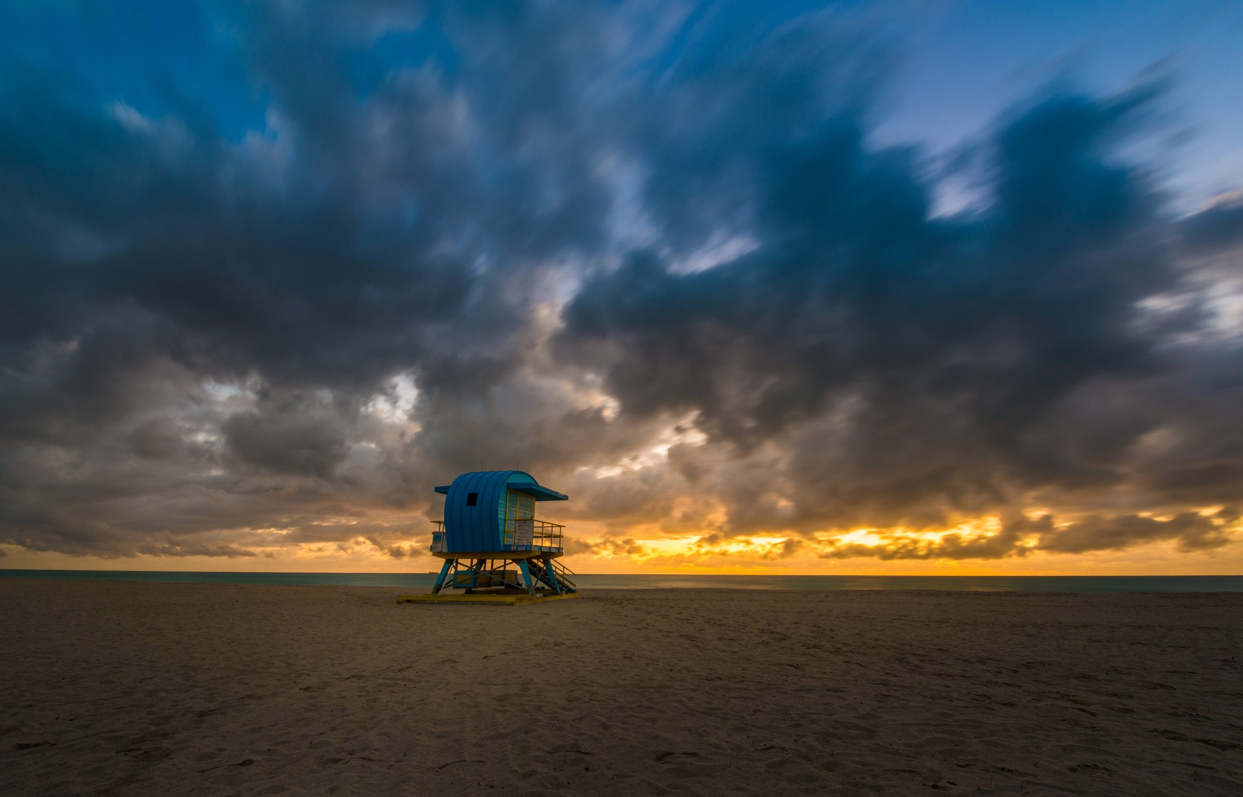 Dark storm clouds over a blue lifeguard stand on an empty beach at last light with a strip of gold on the horizon
