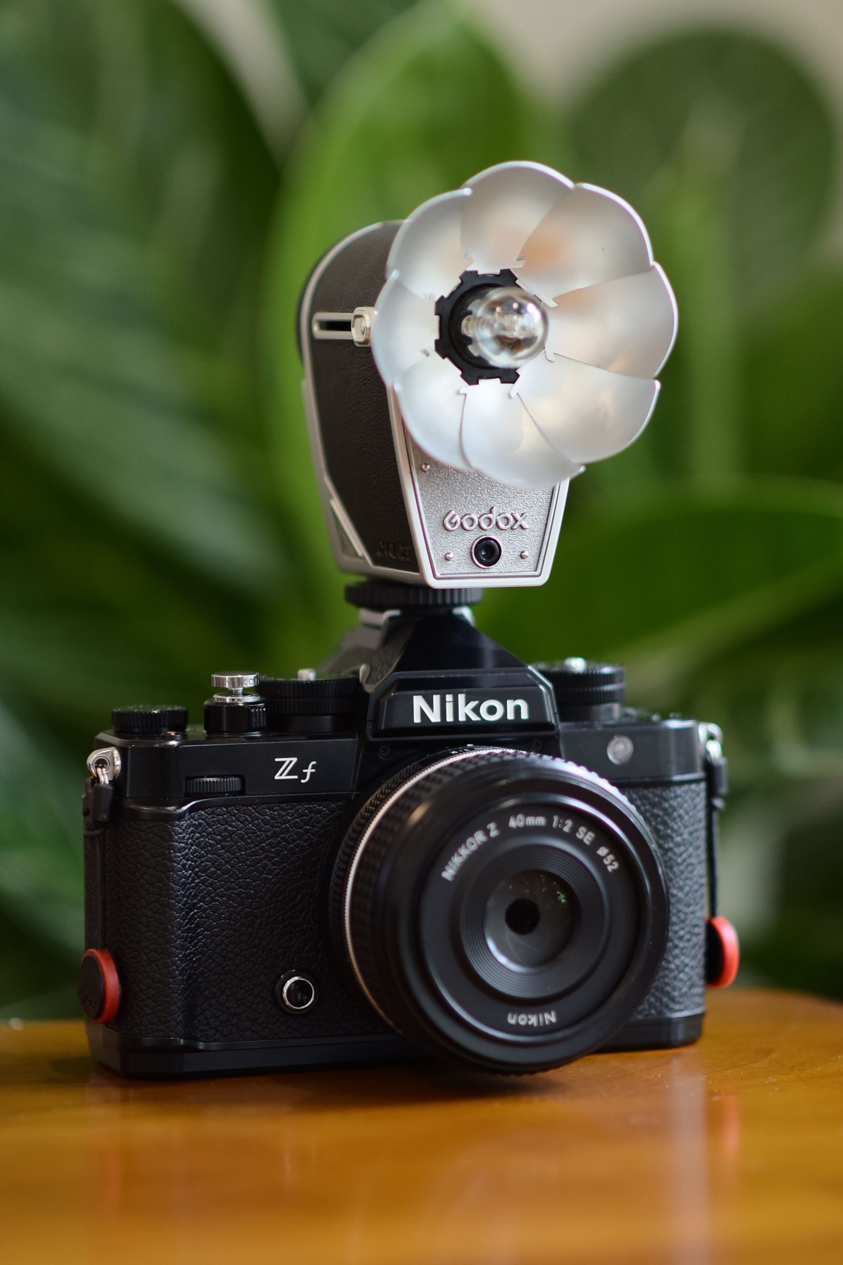 A Nikon Zf camera with a Godox flash mounted, on a table outdoors